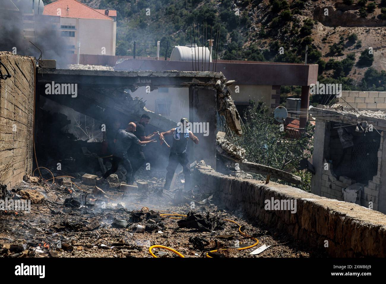 Shebaa, Libano. 18 agosto 2024. La gente cerca di spegnere un incendio in casa colpito da un attacco di droni israeliani nel villaggio di Shebaa al confine con il Libano meridionale. Tre peacekeeper della forza provvisoria delle Nazioni Unite in Libano (UNIFIL) sono stati lievemente feriti in un'esplosione vicino al loro veicolo nelle vicinanze della città meridionale di Yarine. Credito: Stringer/dpa/Alamy Live News Foto Stock