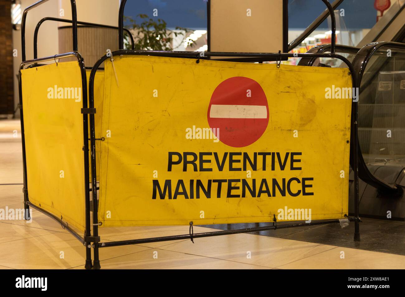 Barriera di sicurezza gialla brillante con scritta nera in grassetto che indica LA MANUTENZIONE PREVENTIVA - intorno all'ingresso di una scala mobile. Presa a Toronto, Canada. Foto Stock