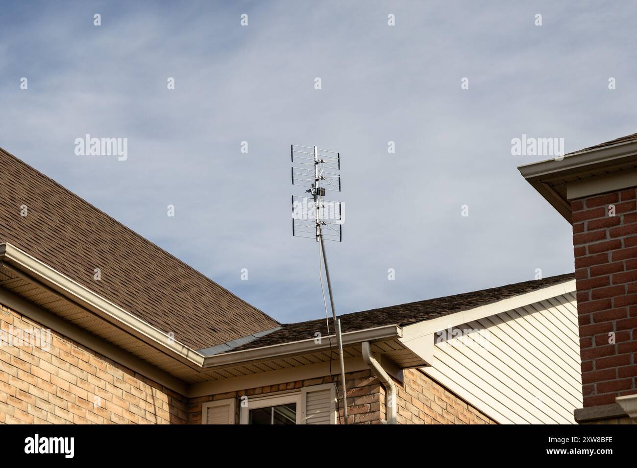 Sfondo blu chiaro con un'antenna Yagi multi-elemento montata sul tetto - casa residenziale in mattoni. Presa a Toronto, Canada. Foto Stock