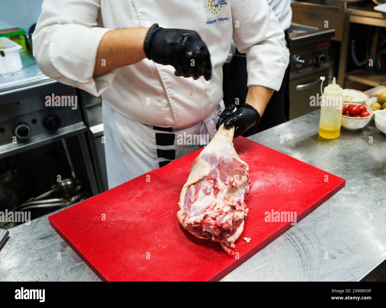 Lo chef prepara anche piatti di agnello. Il processo di cottura stinco di agnello chef maschio in una cucina professionale. Cucinare la carne in un ristorante caucasico Foto Stock