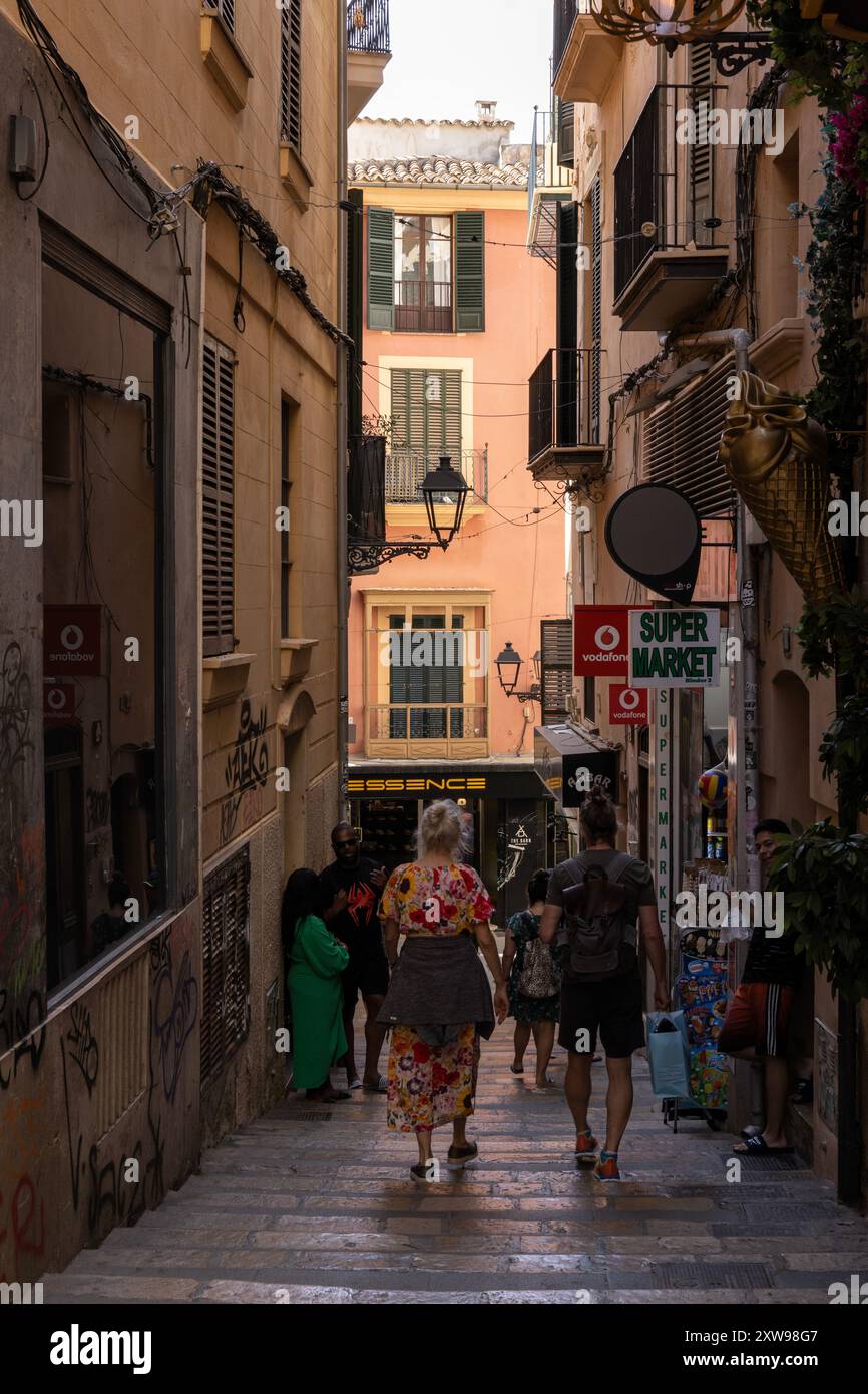 Colorata strada della città vecchia a Palma, Maiorca, fiancheggiata da negozi e case vivaci, piena di turisti rilassati che si godono l'atmosfera estiva. Foto Stock