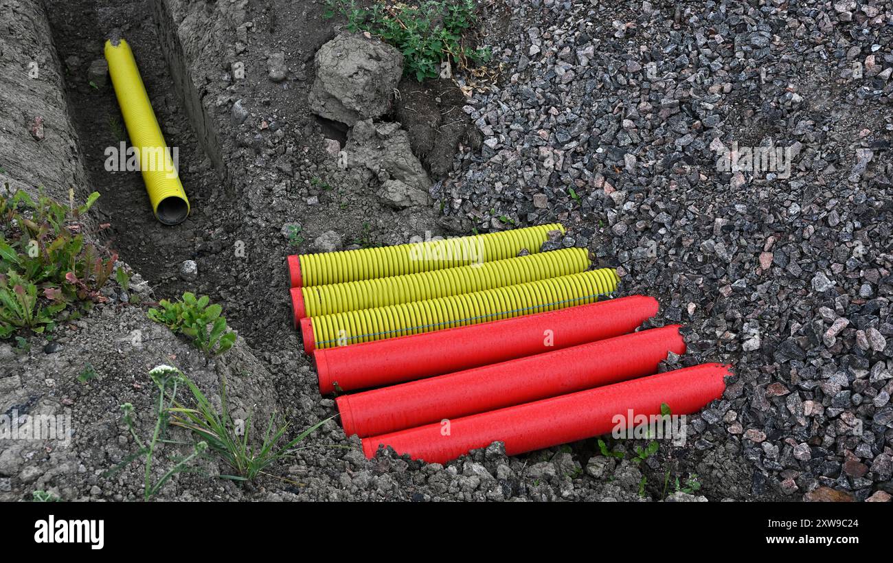 L'immagine cattura un cantiere in cui i tubi corrugati gialli e rossi luminosi sono disposti a terra accanto a una trincea. Il contrasto tra Foto Stock
