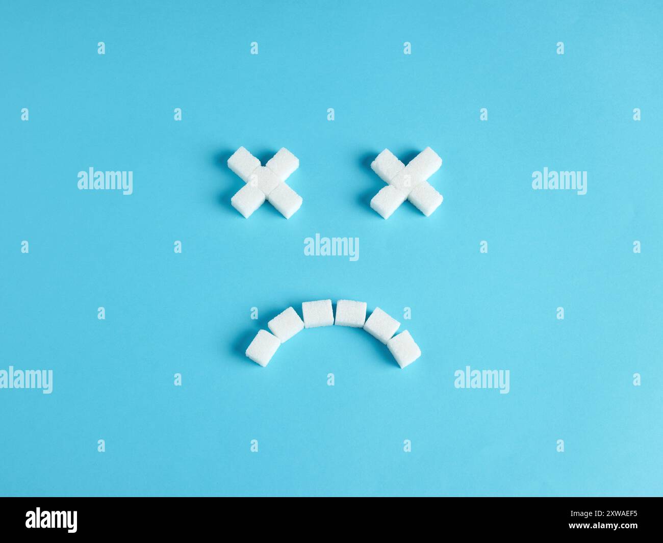 Consumo eccessivo di zucchero. Pericoli di un eccessivo apporto di zucchero. Rischio di diabete e problemi di salute. Faccia sorridente di emoticon morta fatta di cubetti di zucchero su blu Foto Stock