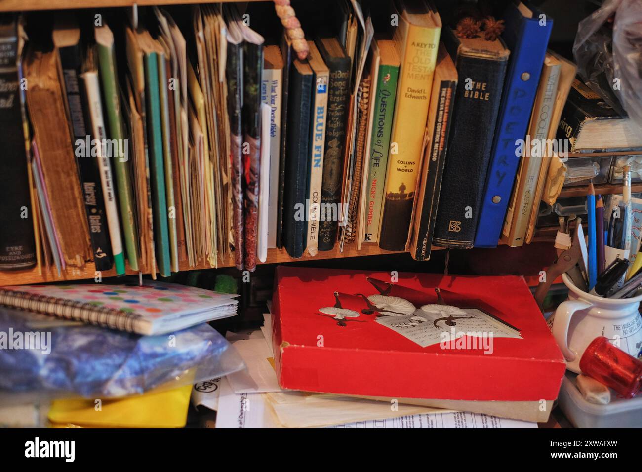 Una vecchia scatola di cioccolato rossa con ballerine, colonne sonore sbiadite, carte, quaderni e matite in una tazza, i genitori anziani che vivono a casa nel disordine del baby boomer Foto Stock