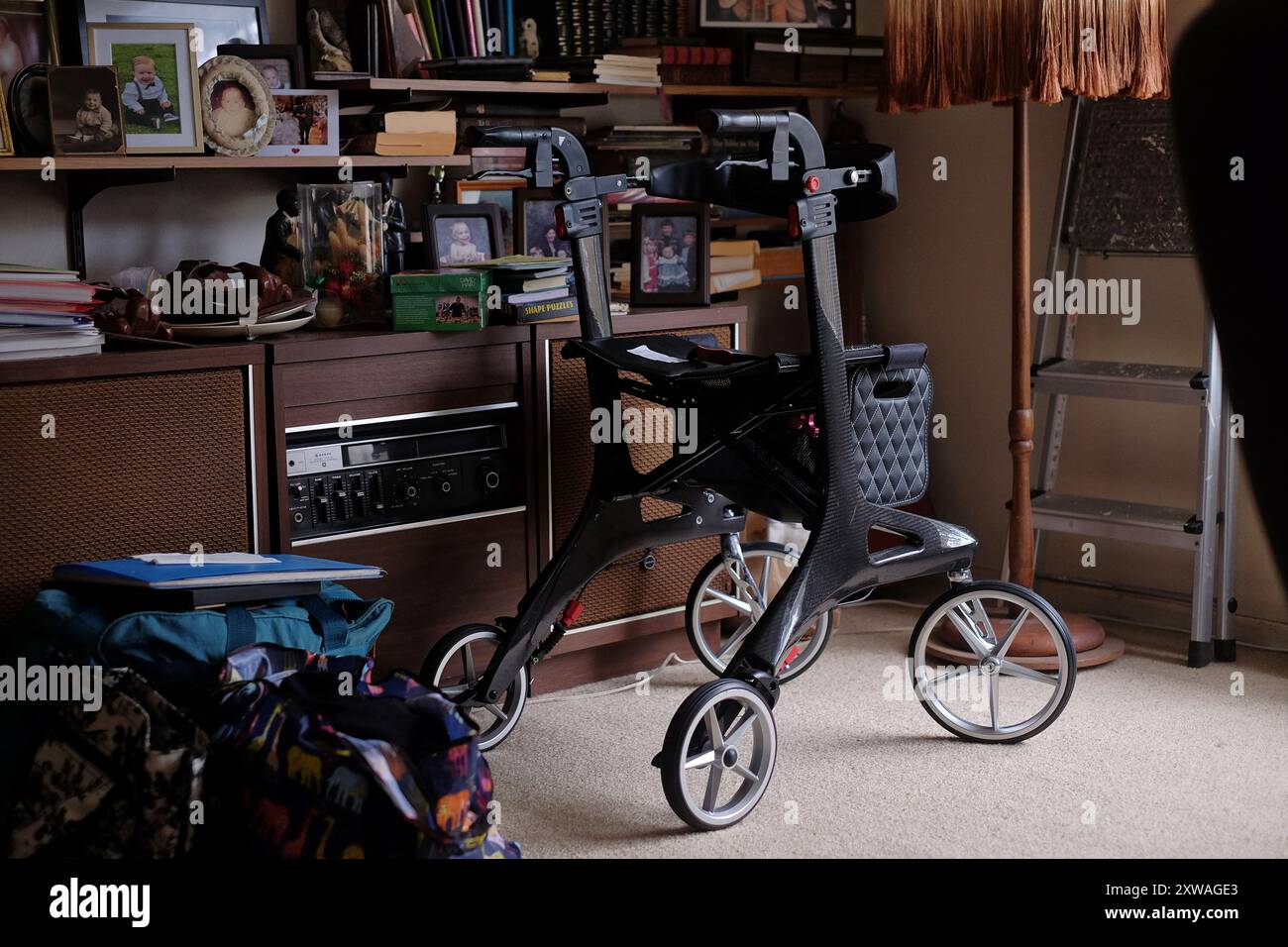 Un camminatore in fibra di carbonio in una sala con un radiogramma e scaffali di fotografie di famiglia incorniciate e libri di anziani che vivono a casa Foto Stock