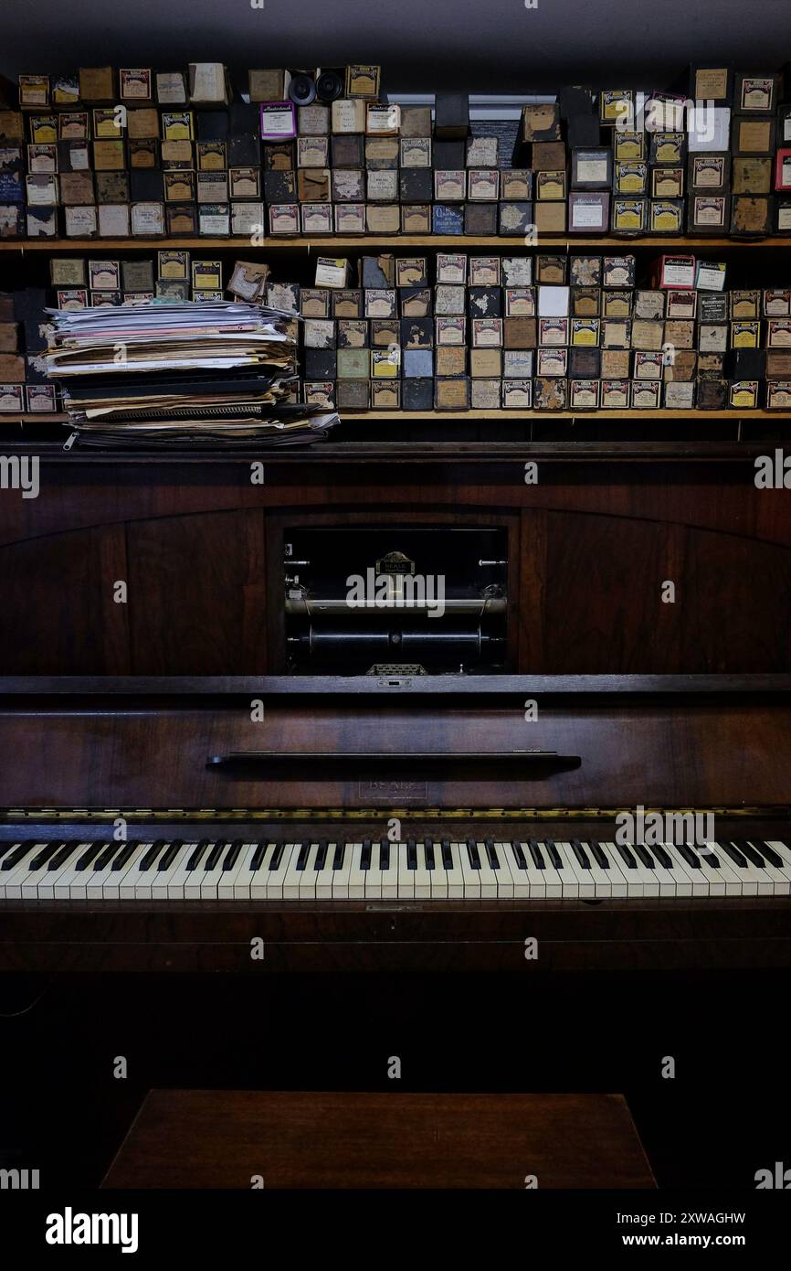 Un pianoforte suonatore con la lavagna e il mobile rotoli aperti con una collezione di rotoli di pianola impilati dieci rotoli alti della larghezza del pianoforte Foto Stock