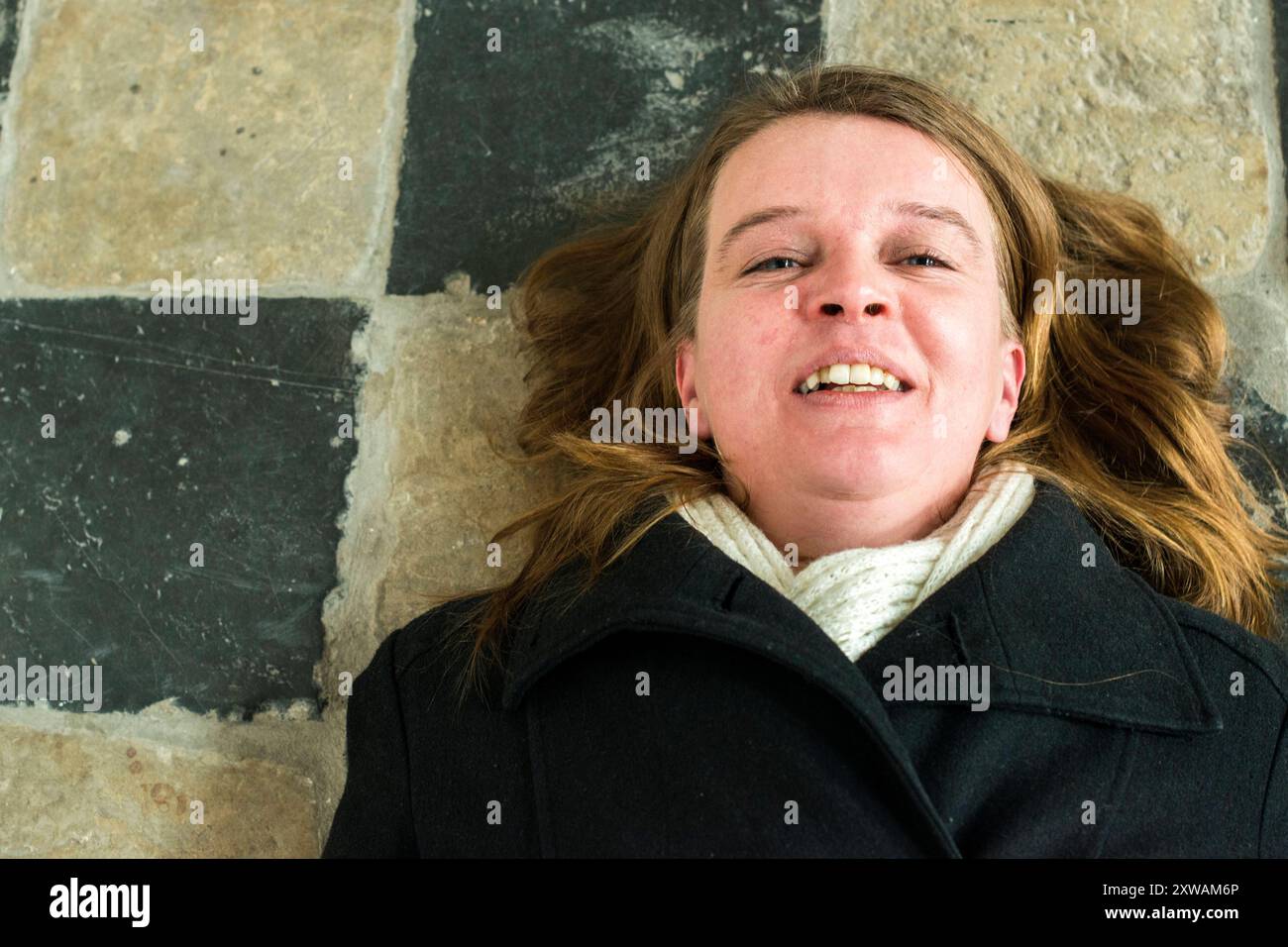 Ritrattista Breda, Paesi Bassi. Donna caucasica media adulta sdraiata su un pavimento mediavale della chiesa mentre sorride con gioia. Breda Down Town Noord-Brabant Nederland Copyright: XGuidoxKoppesxPhotox Foto Stock