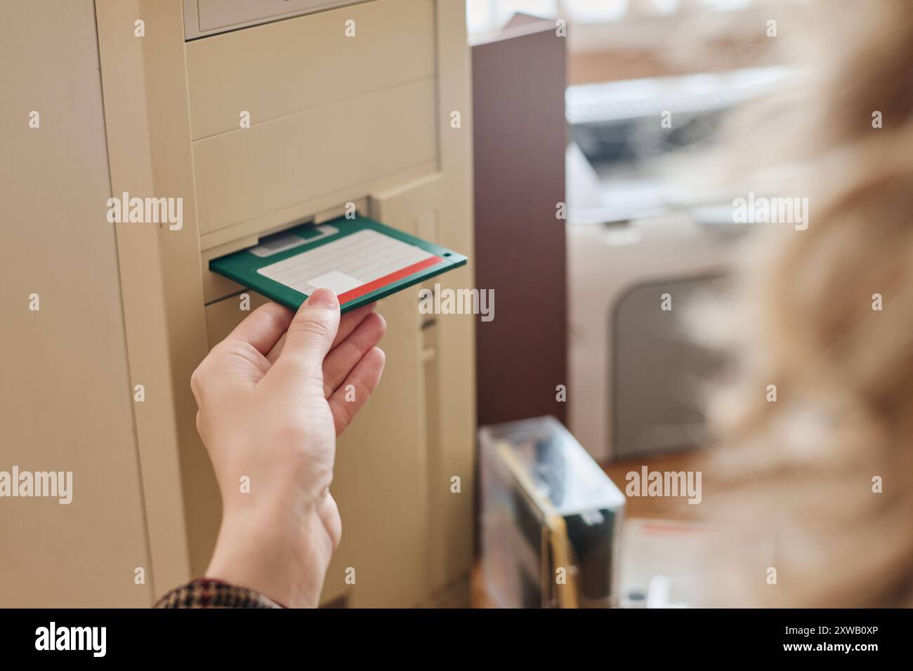 Inserimento manuale di un floppy disk nello slot per unità di un computer vintage, per catturare il momento nostalgico della prima tecnologia informatica, mostrando metodi di archiviazione dei dati obsoleti Foto Stock