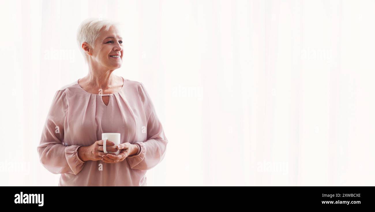 Malinconici old Lady con la tazza di stare accanto alla finestra Foto Stock