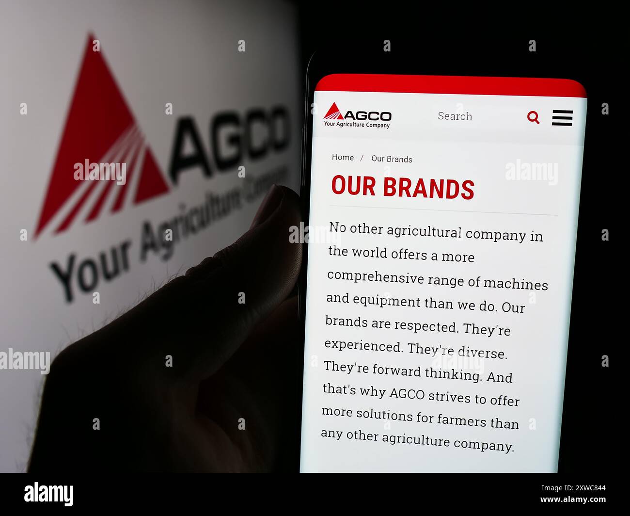 Persona che tiene un cellulare con la pagina Web della società di macchine agricole AGCO Corporation davanti al logo. Messa a fuoco al centro del display del telefono. Foto Stock