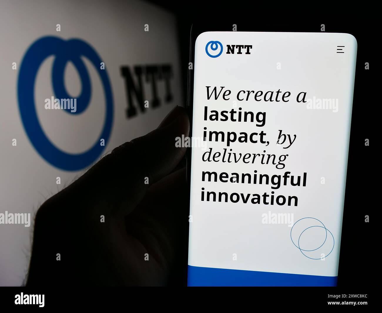 Persona che detiene un cellulare con pagina web della società Nippon Telegraph and Telephone Corporation (NTT) con logo. Messa a fuoco al centro del display del telefono. Foto Stock