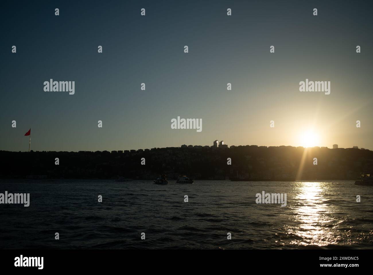 Una vista mozzafiato del Bosforo di Istanbul al tramonto, con l'iconica bandiera turca che sventola orgogliosamente. La luce dorata si riflette sull'acqua, Hig Foto Stock