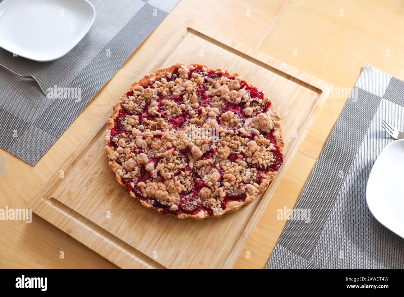 Una torta sbriciolata di prugne fatta in casa su un tavolo di legno al centro di un tavolo da pranzo. Foto Stock