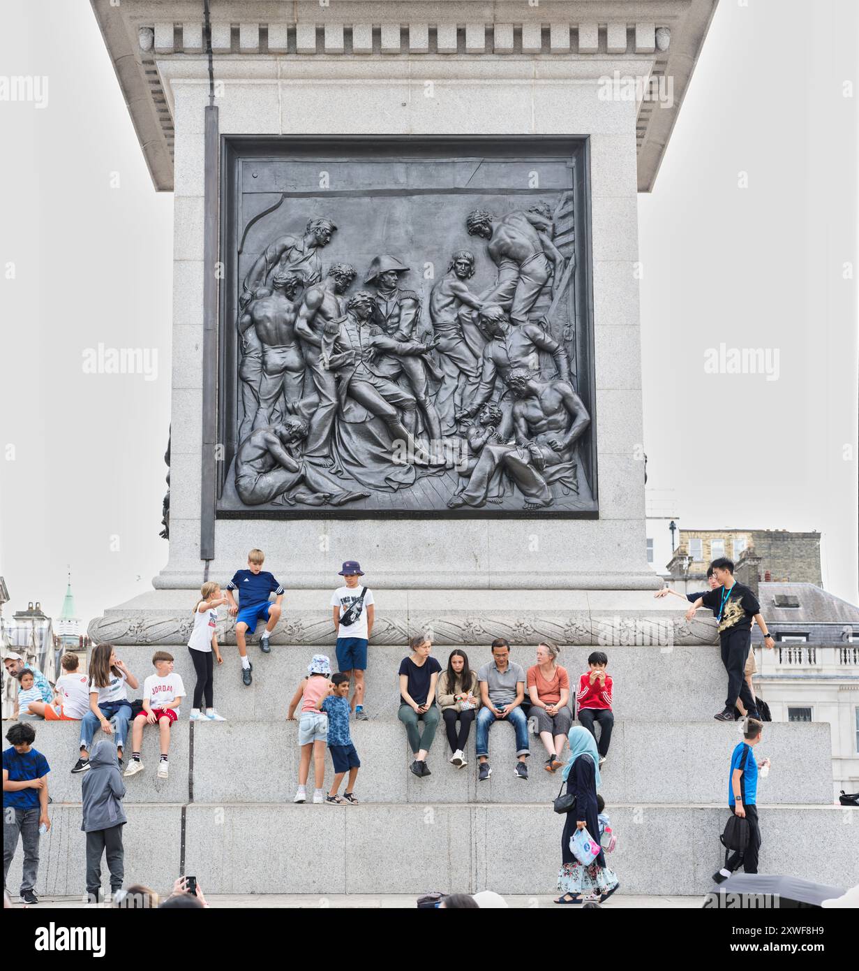 I turisti si siedono sotto la scena della morte dell'ammiraglio Nelson nella battaglia navale di Trafalgar, Nelson Memorial, Trafalgar Square, Londra, Inghilterra. Foto Stock
