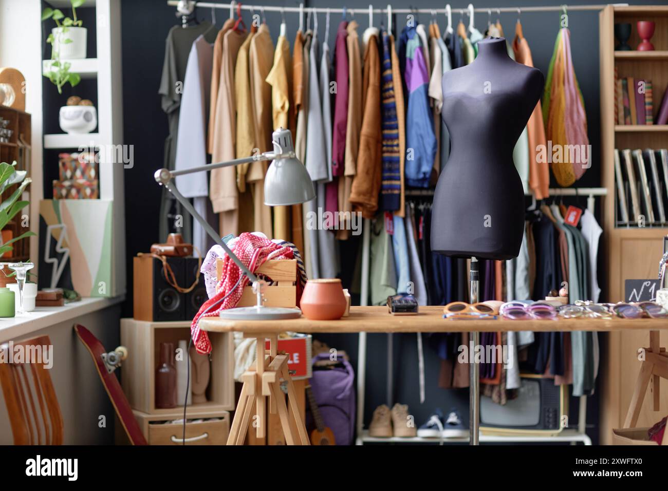 Foto di sfondo del luogo di lavoro dell'addetto alle vendite di un negozio di vendita di thrift con lampada sul tavolo dell'esposizione e manichino accanto ai vestiti appesi su scaffale, spazio per le copie Foto Stock