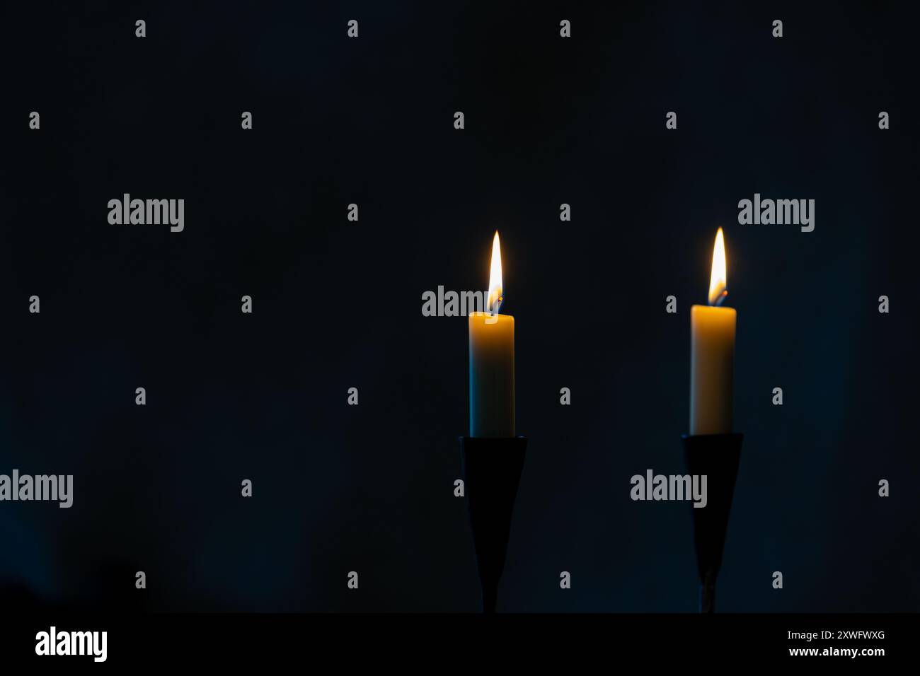 Due candele accese con sfondo blu scuro e spazio di copia Foto Stock
