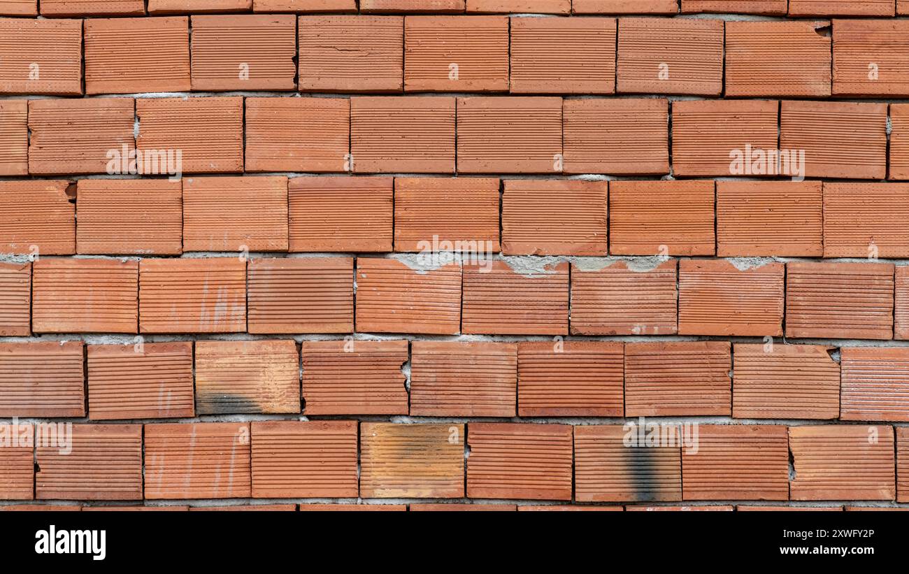Struttura muraria in mattoni rossi di una casa non finita in costruzione, che mostra una superficie ruvida piastrellata. Foto Stock