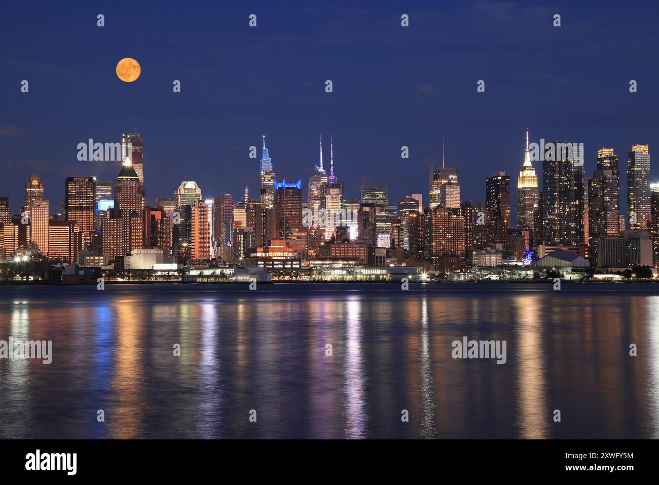 Skyline di New York illuminato al crepuscolo con la luna piena arancione, vista dal fiume Hudson, Stati Uniti Foto Stock