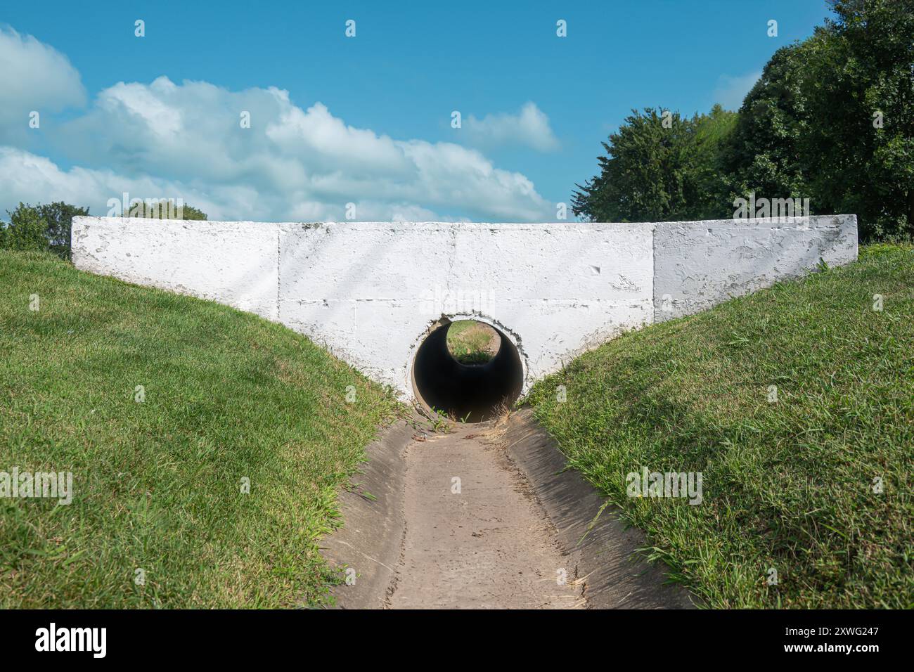 Drenaggio dei canali sotterranei sotto la carreggiata per incanalare grandi quantità di acqua e consentire l'accesso del veicolo sul movimento dell'acqua. La vaschetta d'acqua pavimentata è fiancheggiata dall'erba Foto Stock