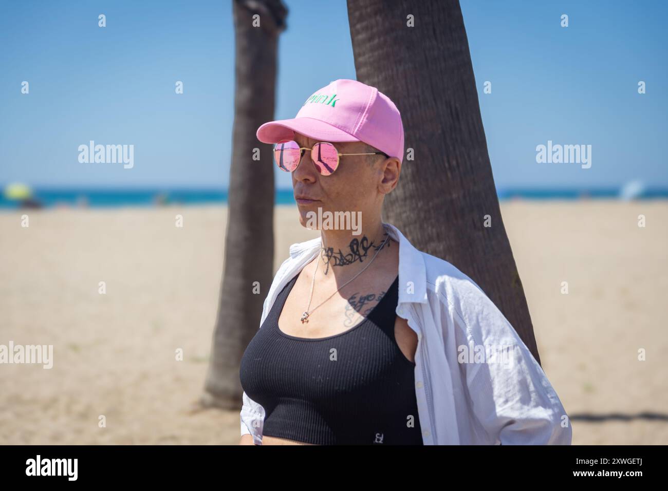 Donna sopravvissuta al cancro su una spiaggia che indossa occhiali da sole e un berretto rosa Foto Stock
