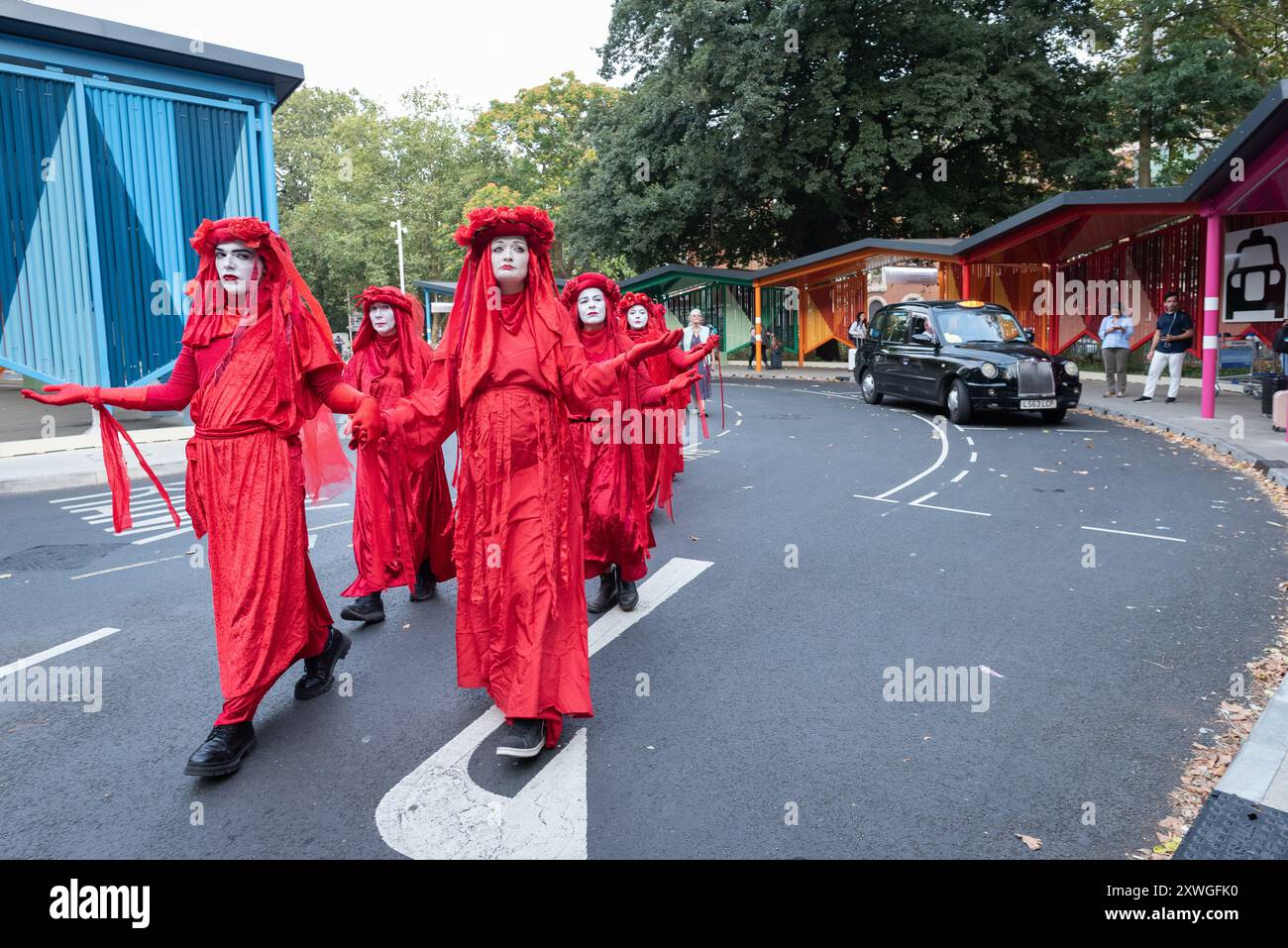 Londra, Regno Unito. 19 agosto 2024. La troupe di mimo attivista della ribellione rossa di Extinction Rebel attraversa Euston Square Gardens, di fronte alla stazione di Euston, in una protesta silenziosa contro gli impatti ambientali del progetto ferroviario HS2, inclusa la perdita di alberi e spazi verdi. L'area, ora un posteggio di taxi, era un tempo un parco pubblico ed è stata occupata da manifestanti in campi e tunnel di alberi nel 2021 nel tentativo di salvarla. Il progetto, il cui futuro è incerto, ha superato enormemente il bilancio e ha causato enormi sconvolgimenti nella zona. Crediti: Ron Fassbender/Alamy Live News Foto Stock