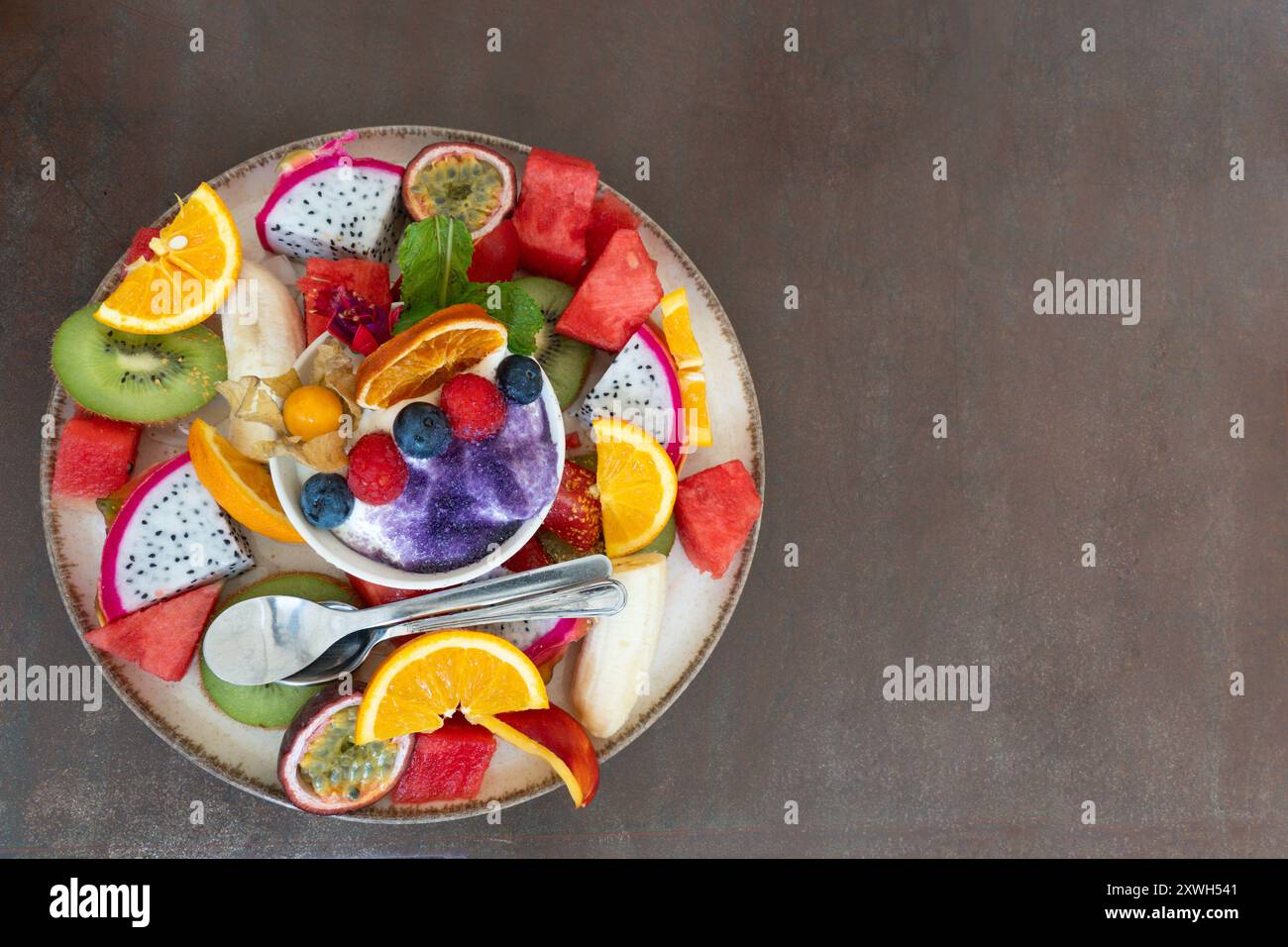 Piatto colorato con pezzi di frutta mista e piccola ciotola con yogurt su un tavolo Foto Stock