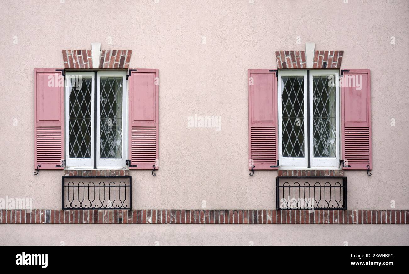 Parete in stucco con finestre con persiane rosa Foto Stock