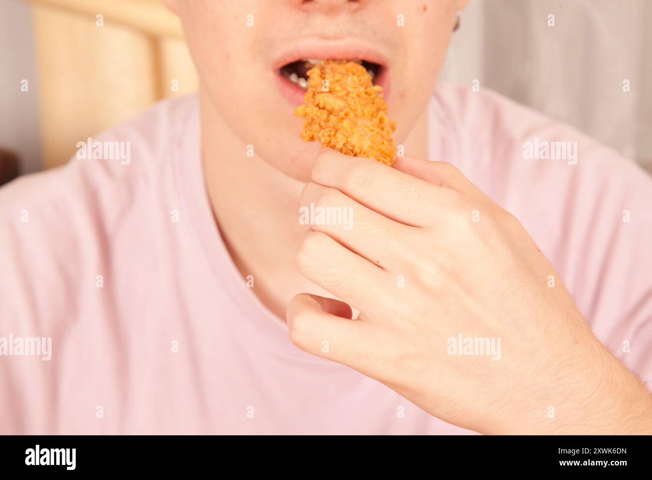 Uomo caucasico che mangia ali di pollo fritte dorate, cultura fast food americana, pezzi di ali di pollo cotti Foto Stock