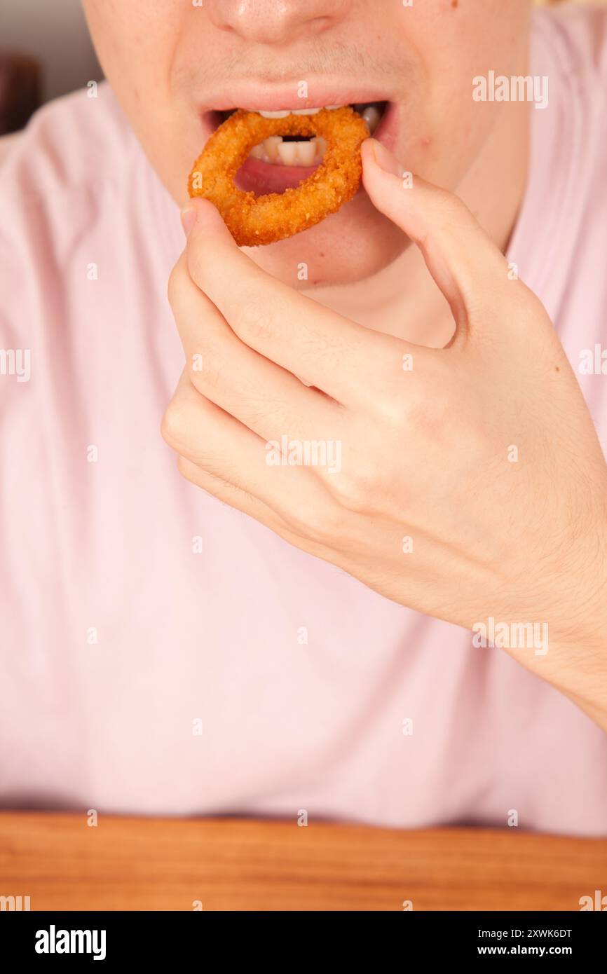 Un uomo caucasico mangia con le mani anelli di cipolla fritti freschi, cultura fast food americana Foto Stock
