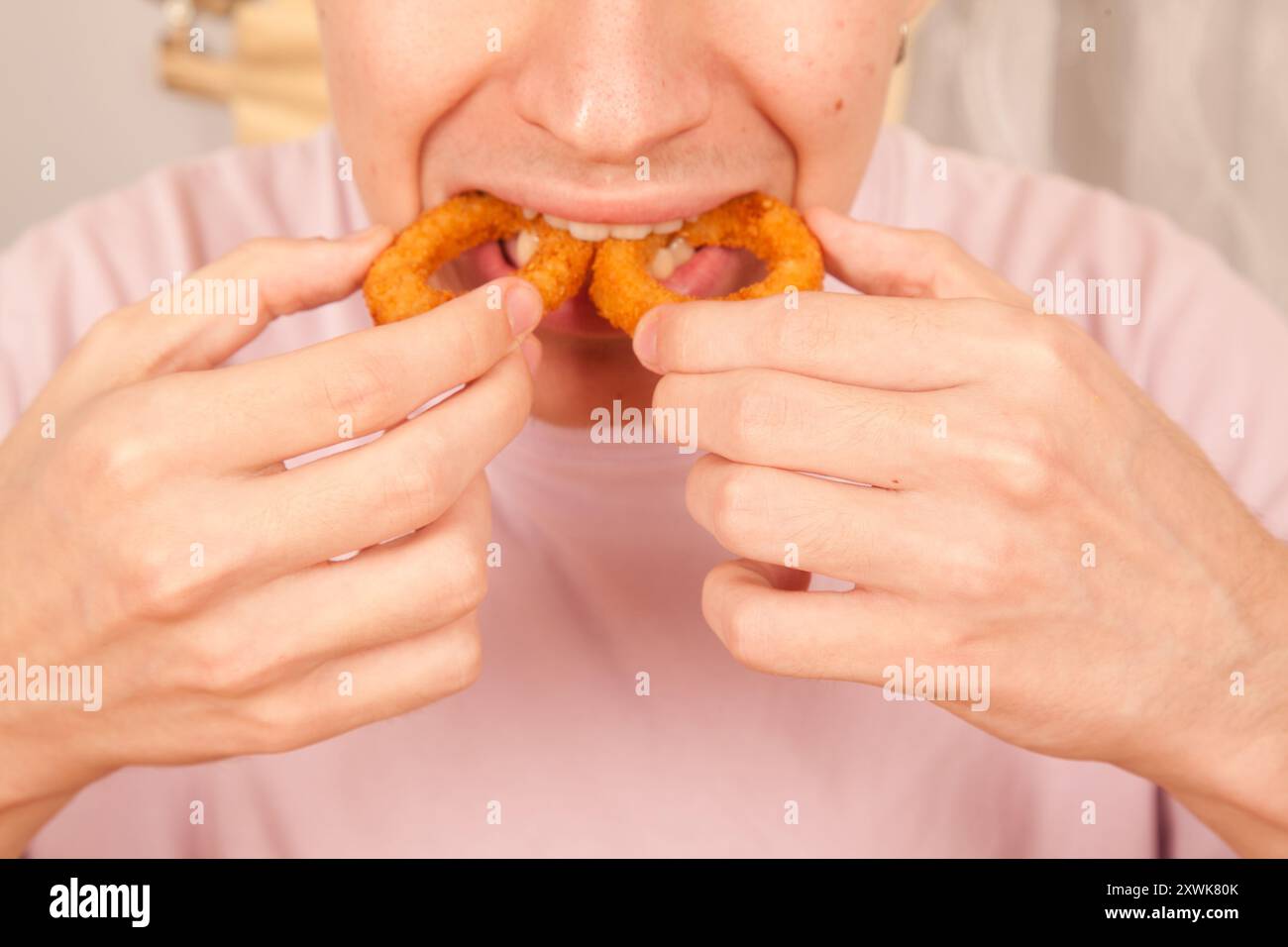 Un uomo caucasico mangia con le mani anelli di cipolla fritti freschi, cultura fast food americana Foto Stock