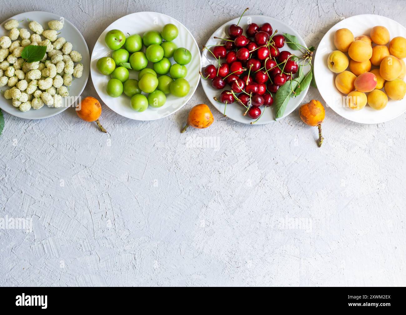 Concetto di frutta estiva, prugne verdi, medlar, albicocche, ciliegie rosse su piatto Foto Stock