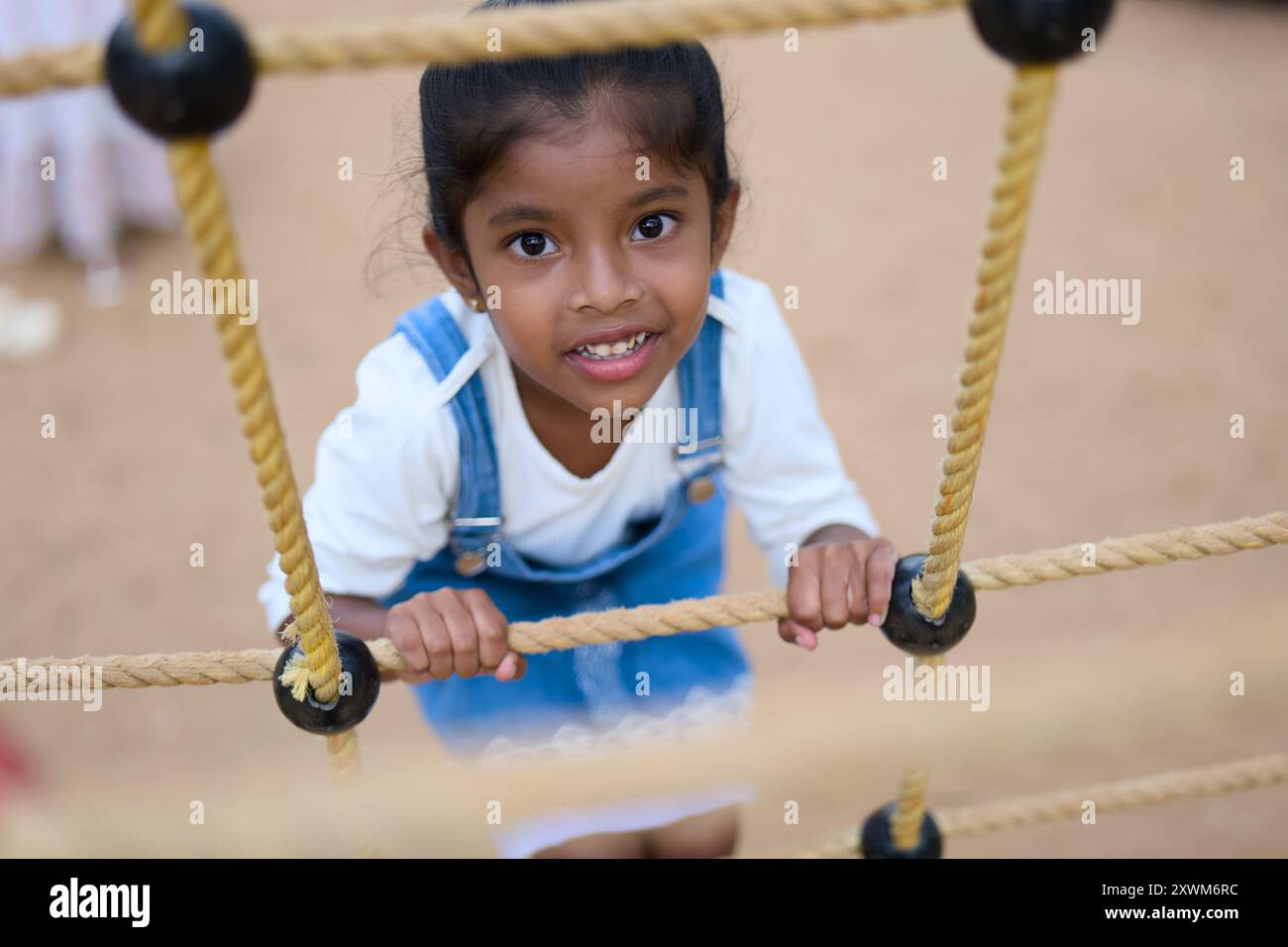 Adorabile ragazza sorride con gioia mentre naviga su una cornice per arrampicarsi su corda al parco giochi. Foto Stock