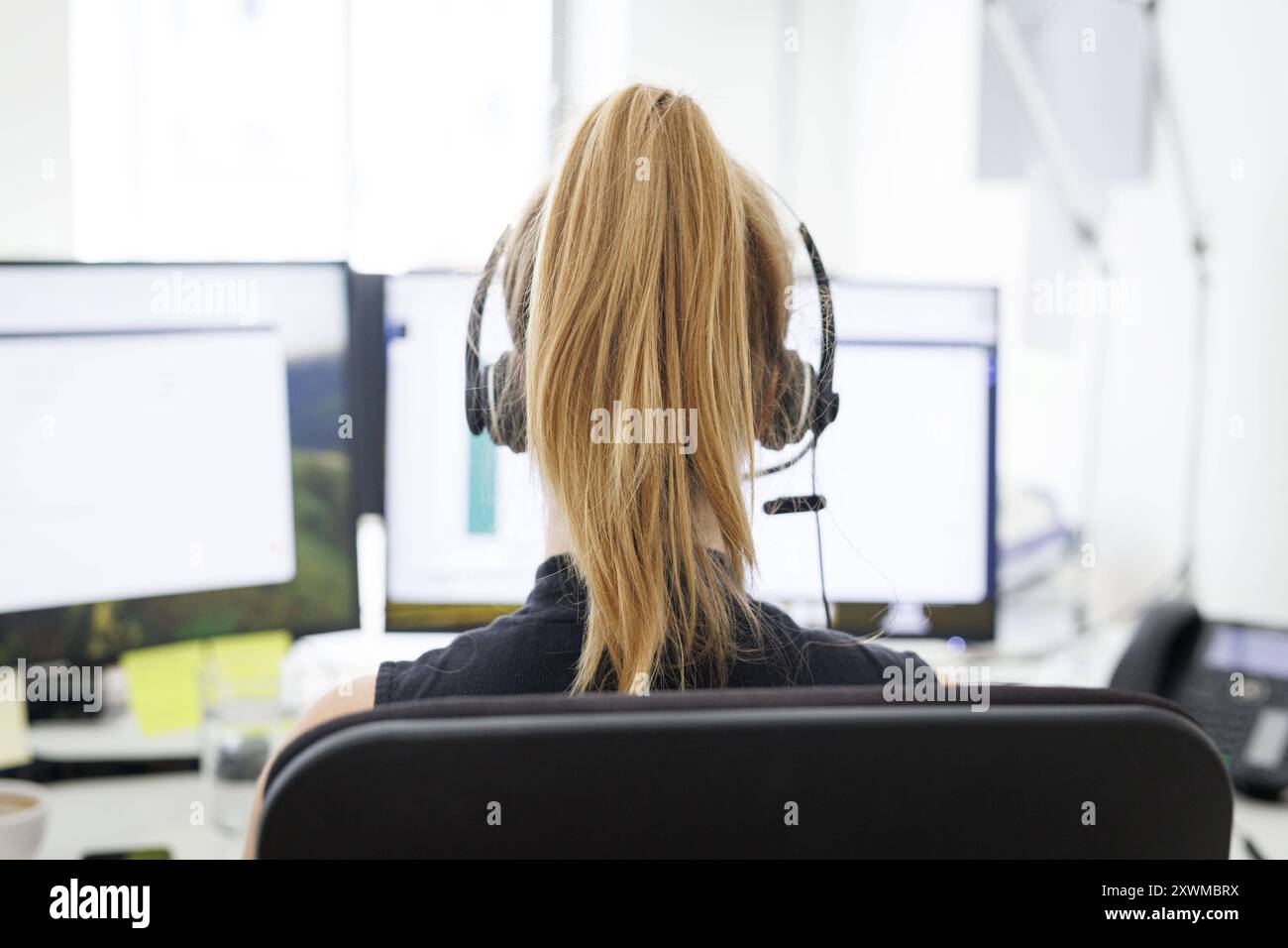 Eine Frau traegt Kopfhoerer in einem Buero a Berlino, 08.08.2024. Arbeit in einem Callcenter Berlin Deutschland *** Una donna indossa le cuffie in un off Foto Stock