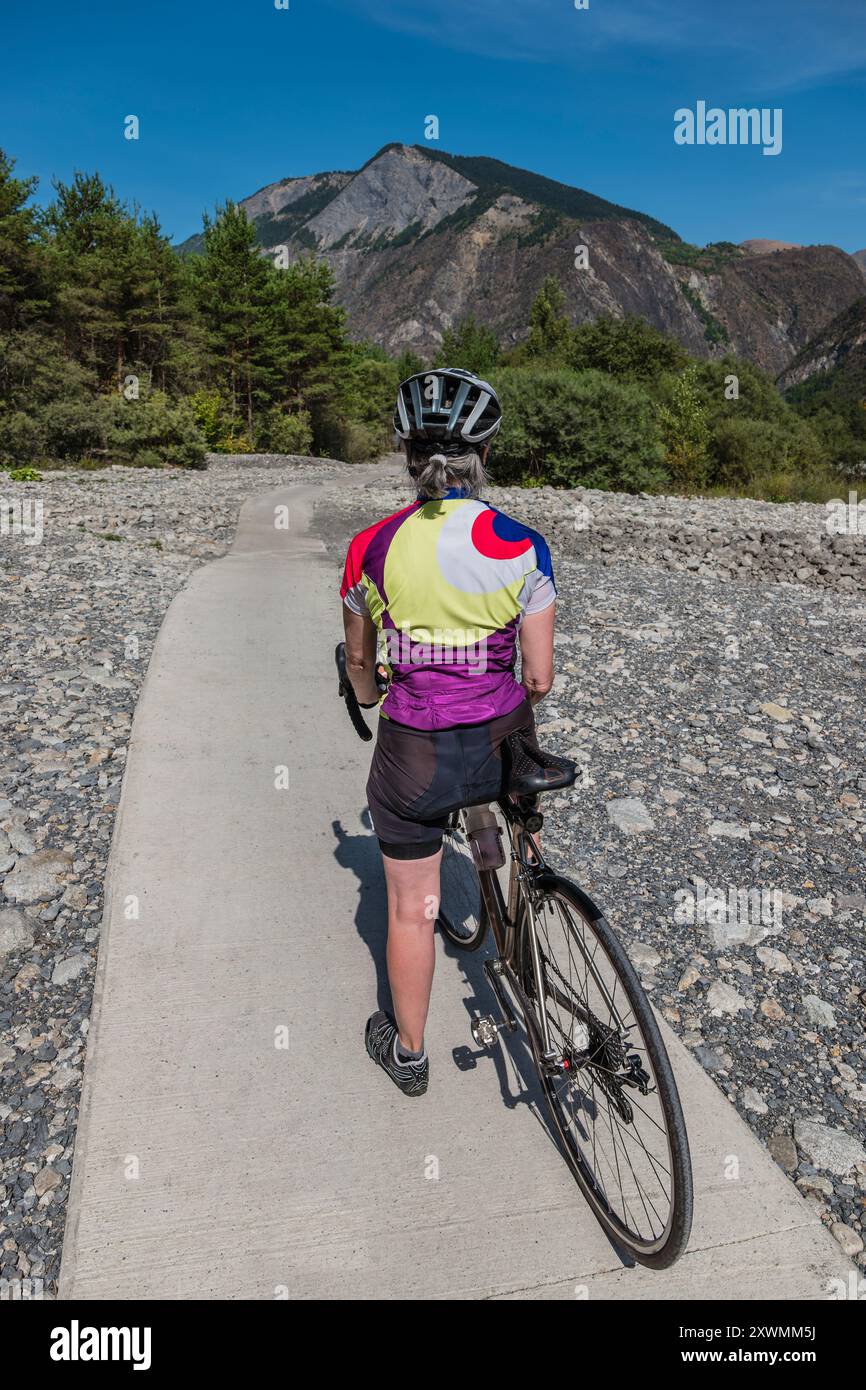 Ciclista donna su una pista attraverso un letto di fiume essiccato nelle Alpi francesi vicino a Bourg d'Oisans. Foto Stock