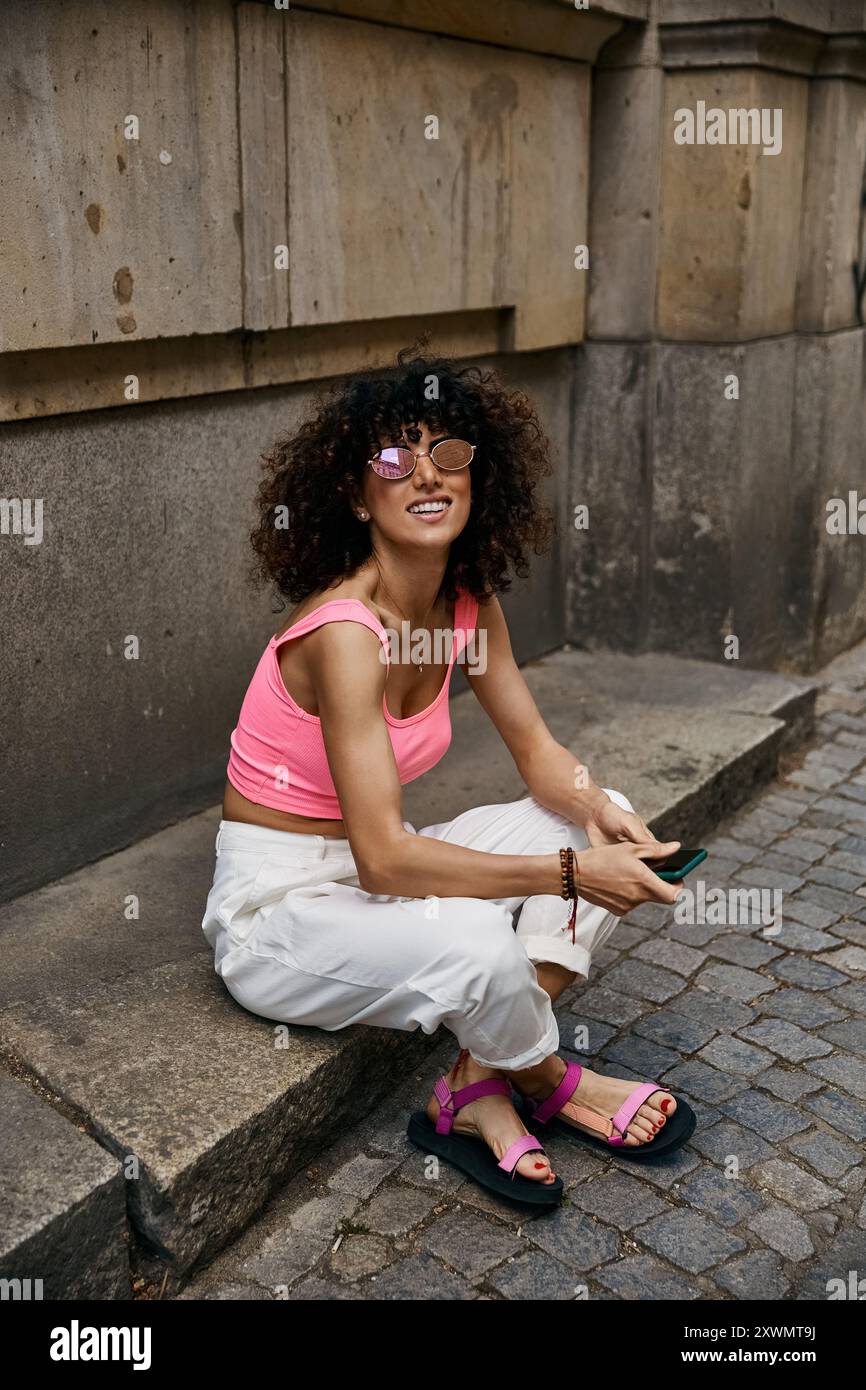 Una donna alla moda con canotta rosa e pantaloni bianchi si trova a un passo in una città europea. Foto Stock Una donna alla moda con canotta rosa e pantaloni bianchi si trova a un passo in una città europea. Foto Stock