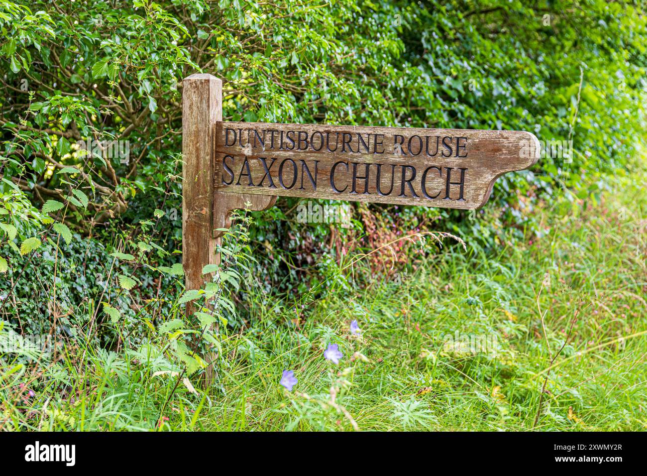 Il cartello in legno che indica la chiesa sassone nel villaggio Cotswold di Duntisbourne Rouse, Gloucestershire, Inghilterra Regno Unito Foto Stock