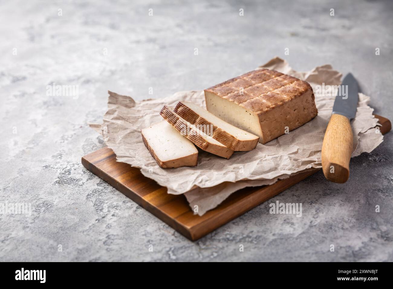 Tofu affumicato biologico sul tavolo della cucina con coltello Foto Stock