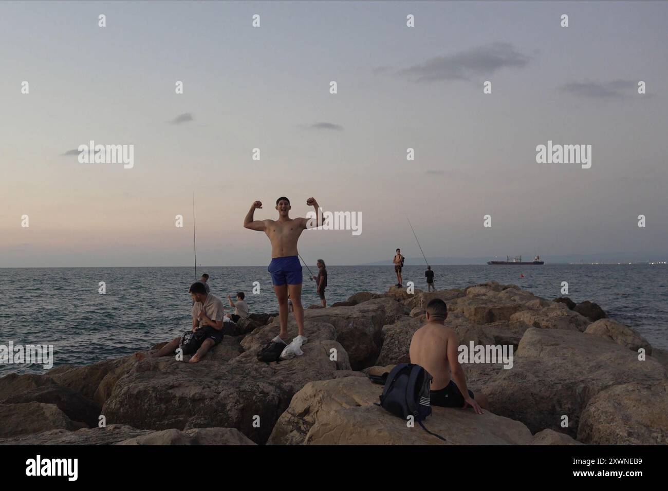 La gente siede su una scogliera rocciosa alla spiaggia di Bat Galim il 14 agosto 2024 ad Haifa, Israele. Foto Stock