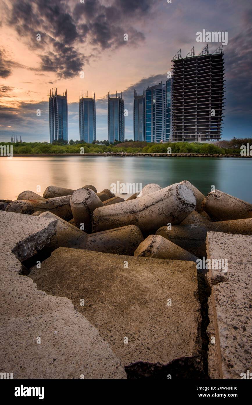 Tetrapodi e lastre di cemento lungo il lungomare con grattacieli sullo sfondo, Indonesia Foto Stock