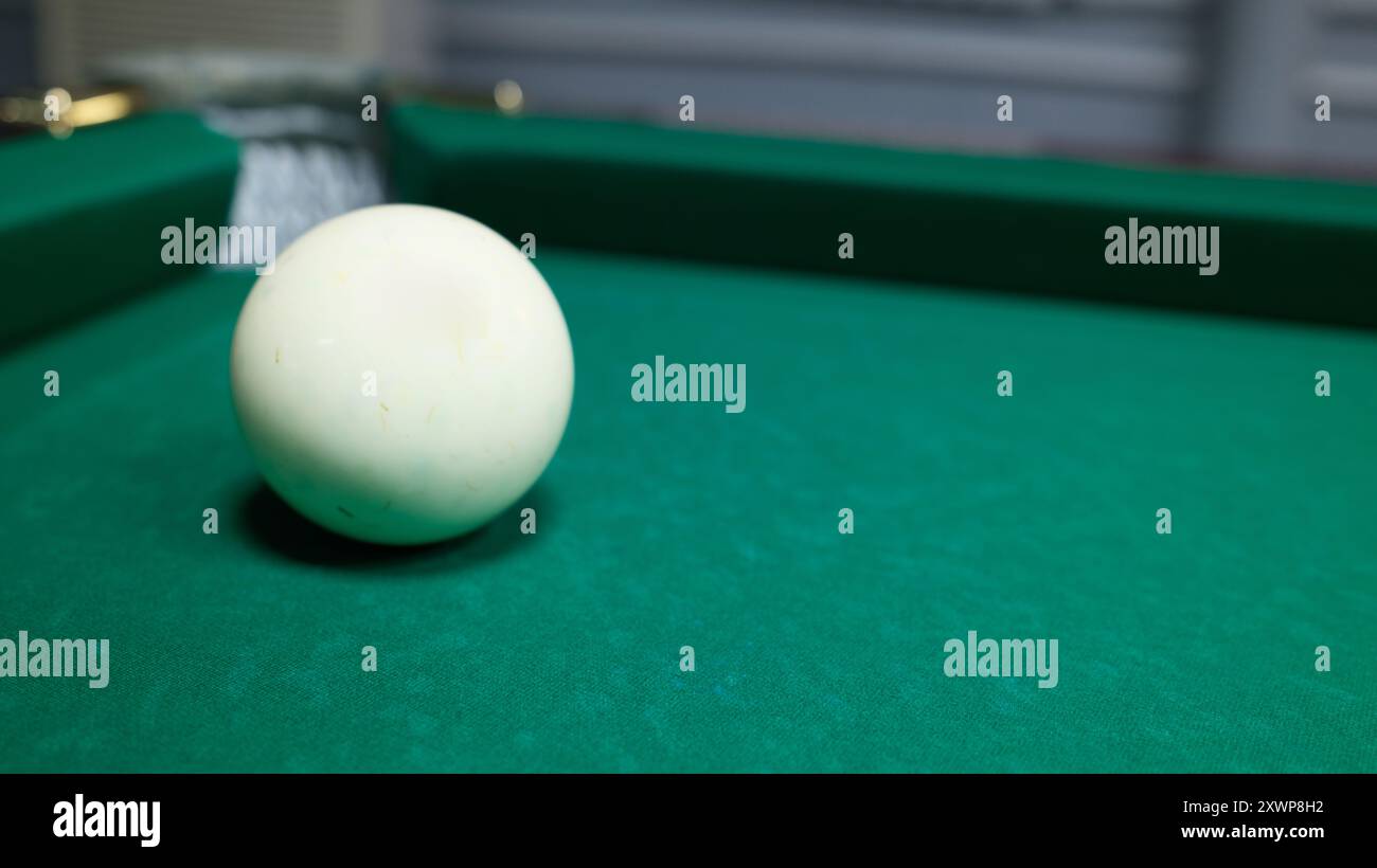 Palla da biliardo bianca singola su un tavolo in feltro verde. Primo piano di CUE ball, attrezzature da biliardo, sport e tema ricreativo. Foto Stock