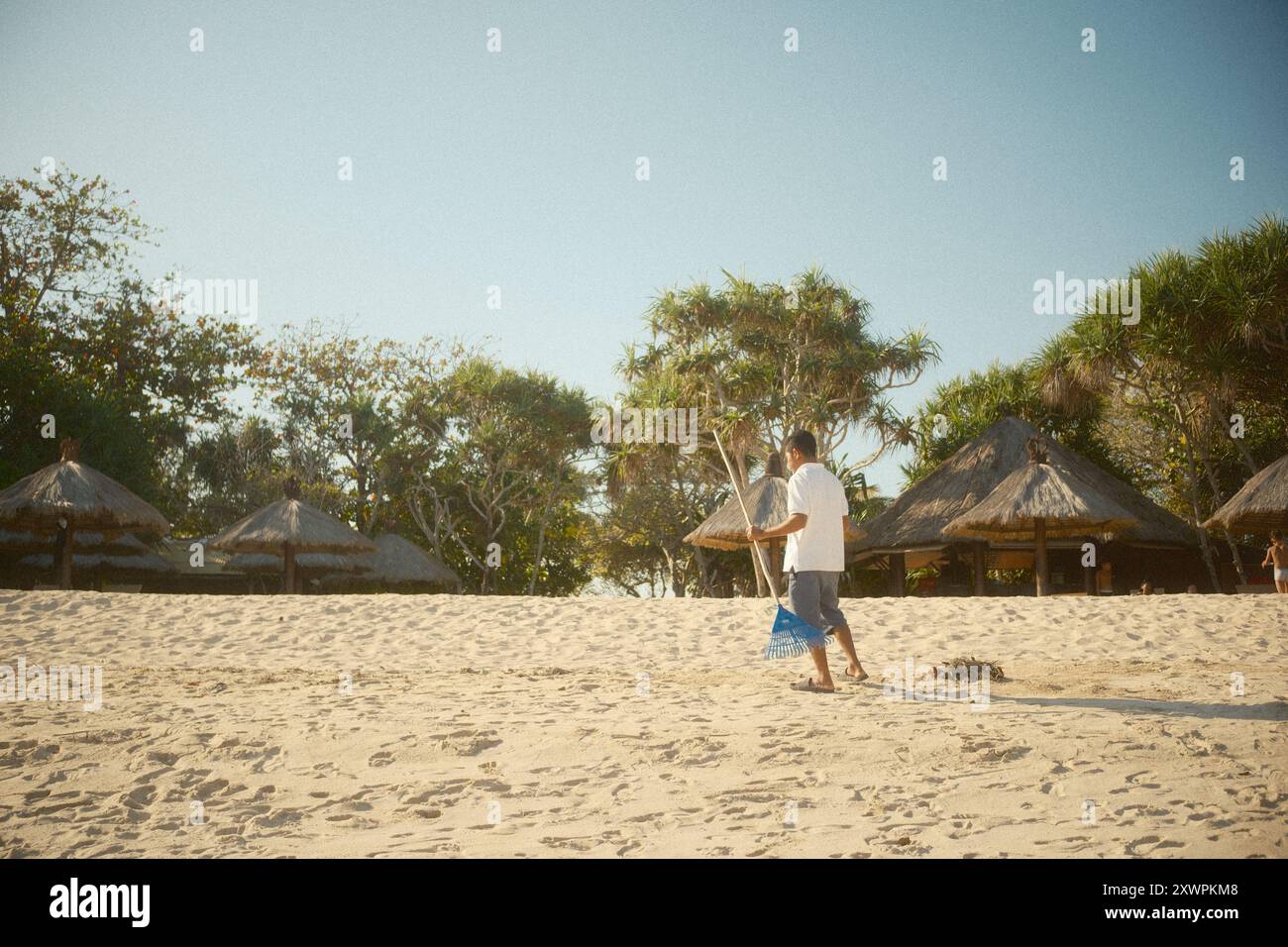 Nusa Dua, Bali, Indonesia - 19 agosto 2024: Il personale addetto alle pulizie della spiaggia sta raccogliendo rifiuti e detriti lungo la costa di fronte a una capanna sulla spiaggia Foto Stock
