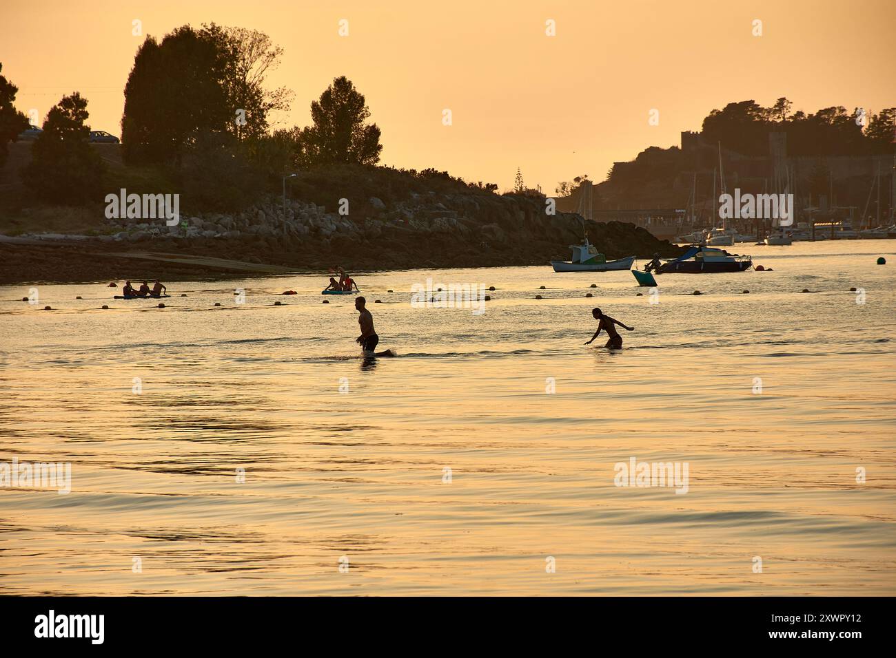 Mentre il giorno sbiadisce nella notte, le sagome dei giovani che giocano e fanno il bagno nelle acque di Ladeira Beach creano un'affascinante e nostalgica sce Foto Stock