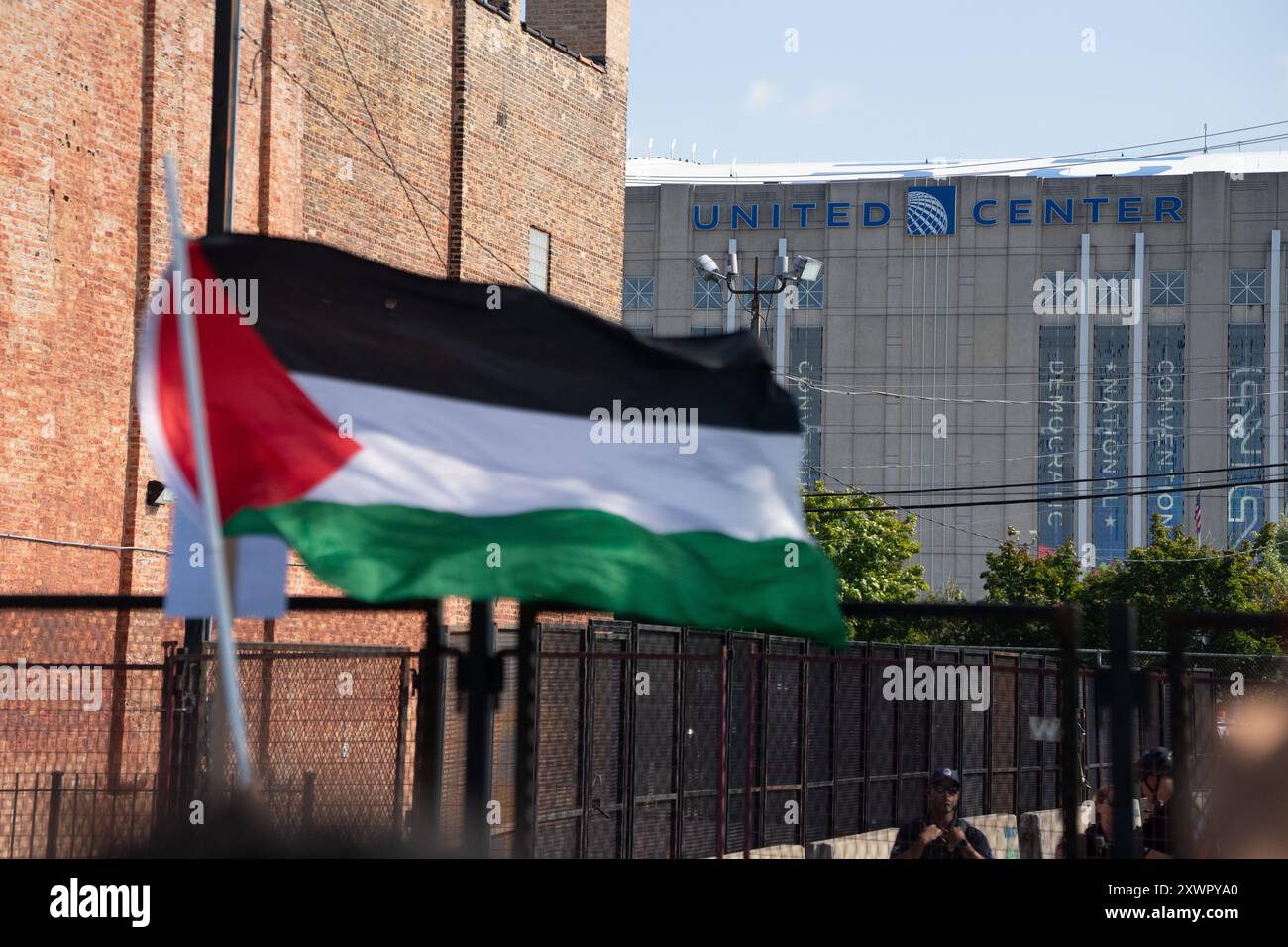 Un manifestante sventola una bandiera palestinese alla scherma intorno allo United Center durante il DNC di Chicago, poco prima che i manifestanti violassero il perimetro. Foto Stock