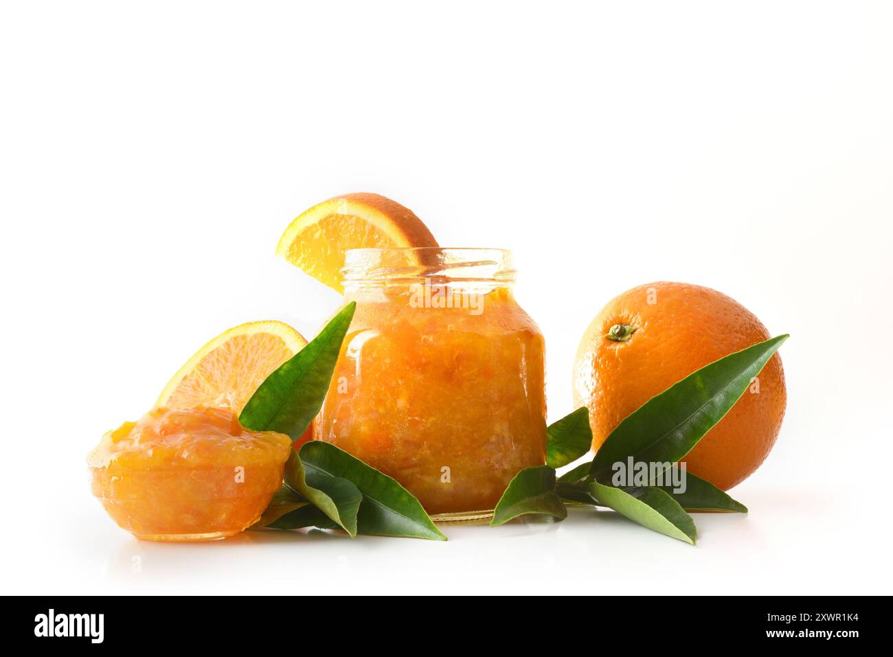 Vasetto di marmellata d'arancia isolato su sfondo bianco con la frutta intorno che si riflette sulla base. Vista frontale. Foto Stock