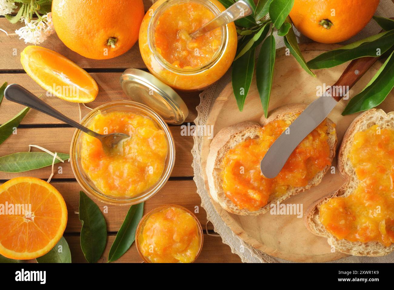 Marmellata d'arancia fatta in casa su fette di pane e vasetti pieni di marmellata e frutta intorno al tavolo di legno. Vista dall'alto. Foto Stock