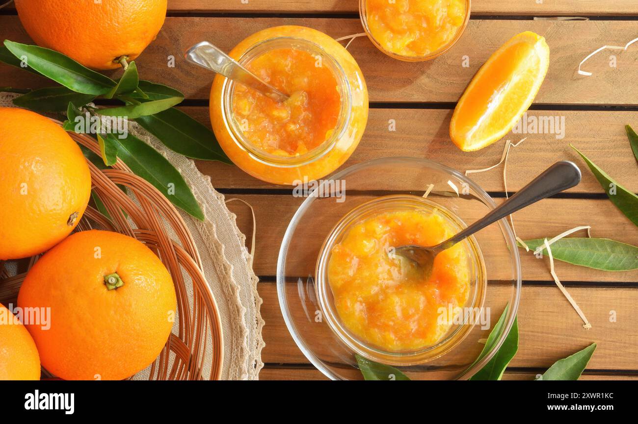 Marmellata d'arancia fatta in casa in vasetti di vetro su un tavolo di legno con pezzi di frutta. Vista dall'alto. Foto Stock