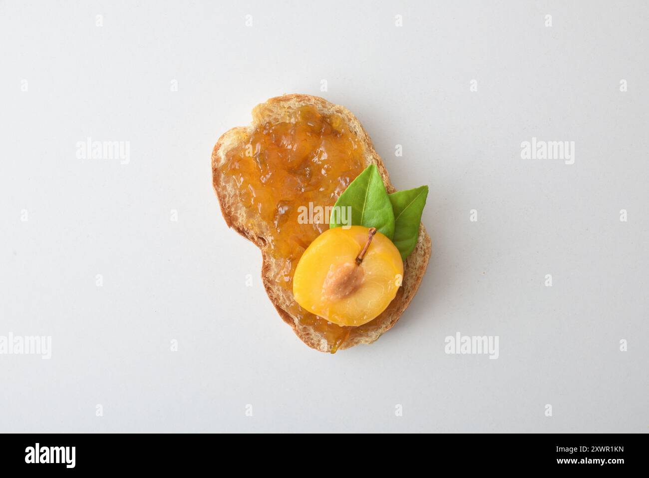 Toast con marmellata di prugne decorata con frutta isolata su un tavolo bianco. Vista dall'alto. Foto Stock
