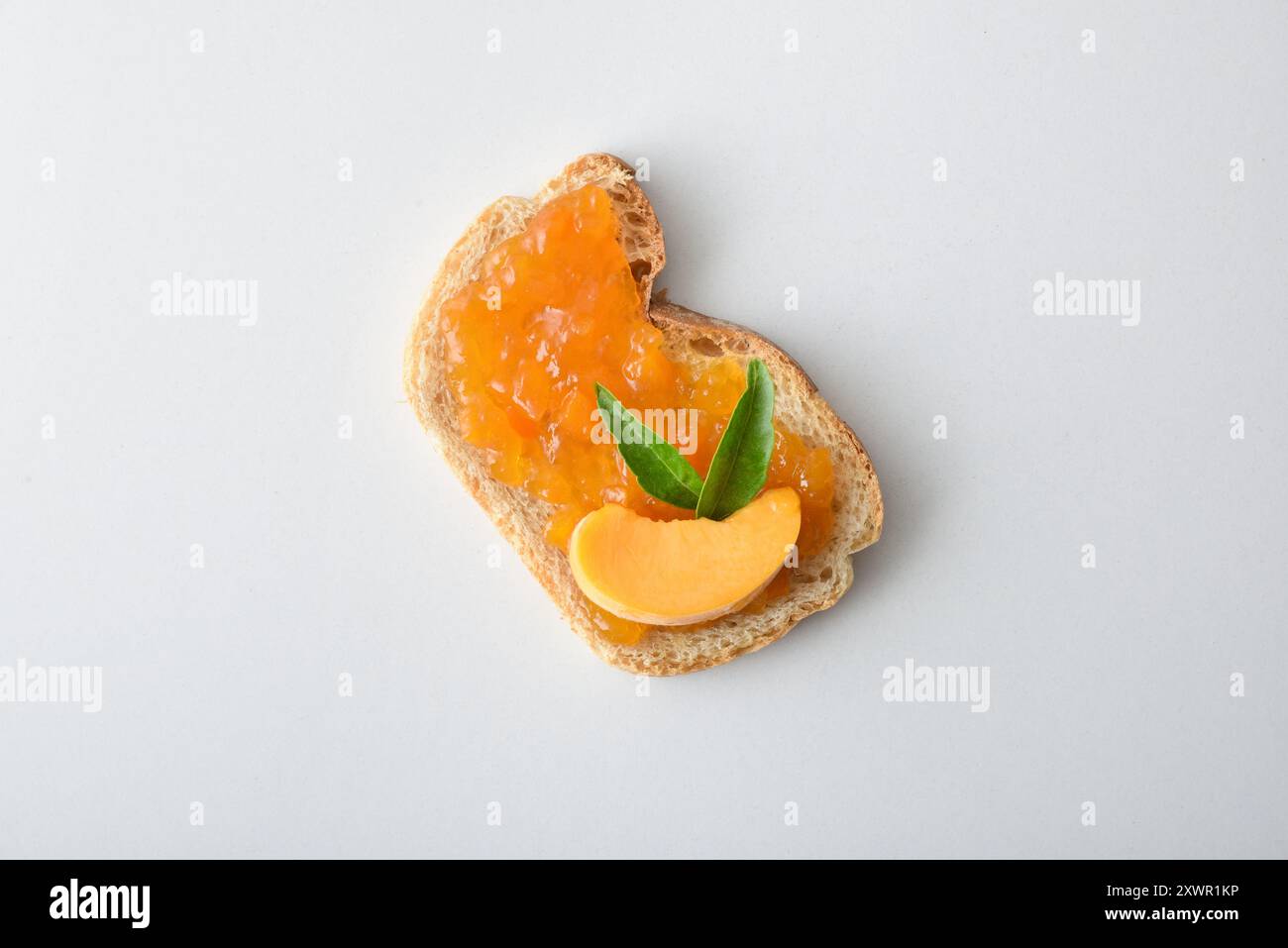 Toast con marmellata di pesca decorata con frutta isolata su un tavolo bianco. Vista dall'alto. Foto Stock