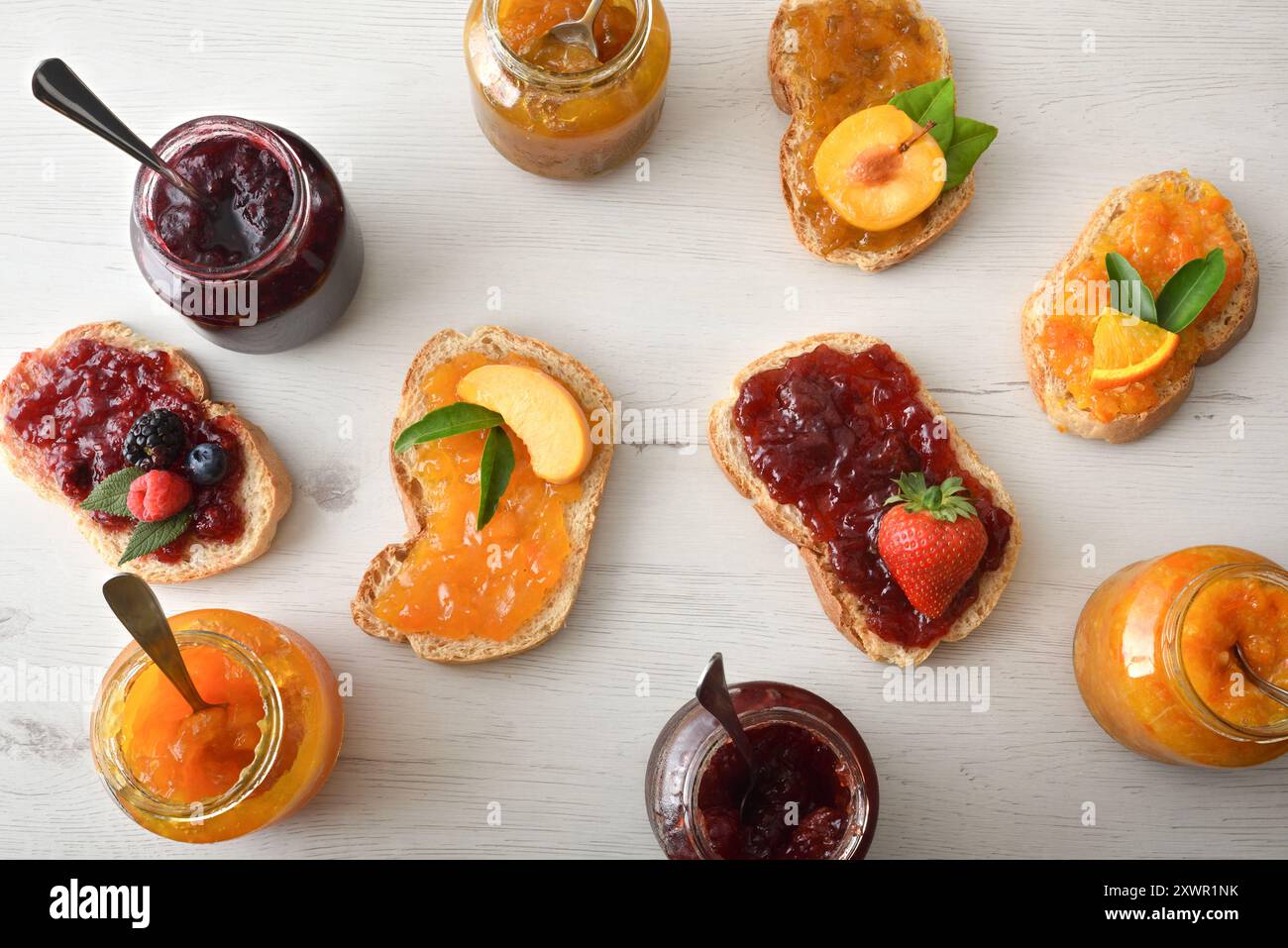 fette di pane con marmellata di vari gusti su un tavolo con vasetti pieni di marmellata. Vista dall'alto. Foto Stock