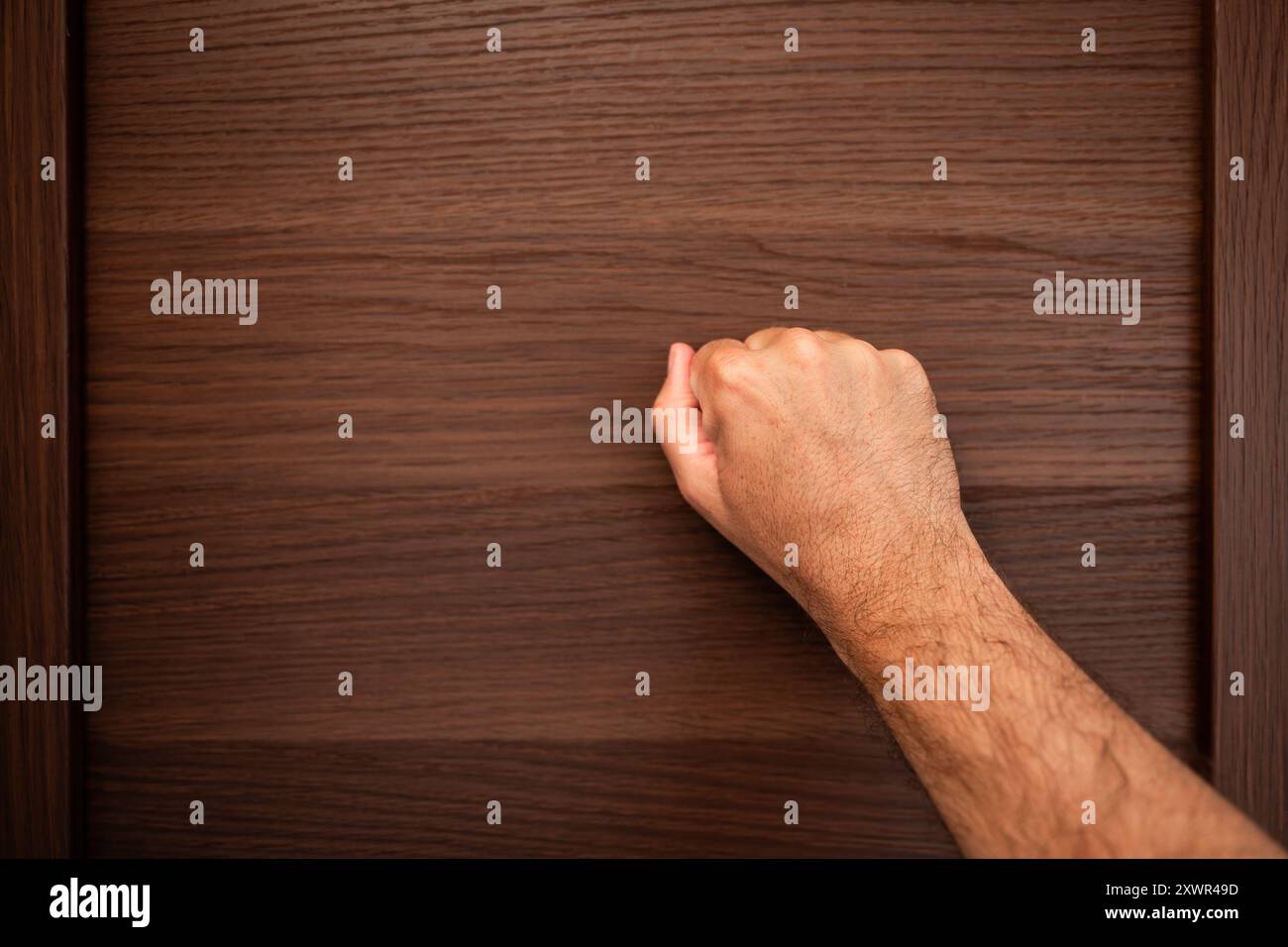 Immagine ravvicinata della mano di una persona che bussa su una porta di legno, simboleggia l'atto di cercare l'ingresso o l'attenzione, con la mano che forma un fi chiuso Foto Stock